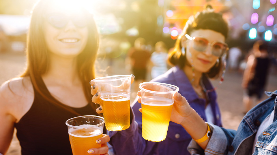 Drei Personen stehen bei sonnigem Wetter zusammen und stoßen mit einem Bierbecher in der Hand an.