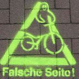 Auf einem Radweg ist ein Warnzeichen mit gelber Farbe aufgetragen worden. Dort ist ein Radfahrer als Geistfigur zu sehen. Darunter steht der Schriftzug "Falsche Seite". Damit sollen sogenannte Geisterradler auf ihr Fehlverhalten hingewiesen werden.