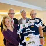 Vier Personen präsentieren feierlich ein Fahrradtrikot, das mit Unterschriften verziert ist.
