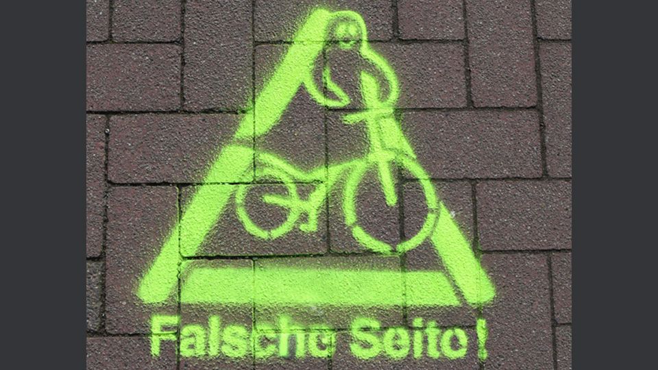 Auf einem Radweg ist ein Warnzeichen mit gelber Farbe aufgetragen worden. Dort ist ein Radfahrer als Geistfigur zu sehen. Darunter steht der Schriftzug "Falsche Seite". Damit sollen sogenannte Geisterradler auf ihr Fehlverhalten hingewiesen werden. 