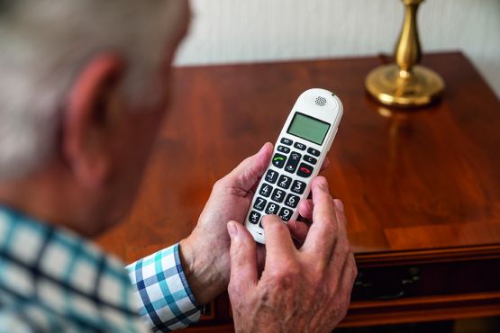 Ein älterer Mann ist von hinten zu sehen, er hält ein Festnetztelefon in den Händen.