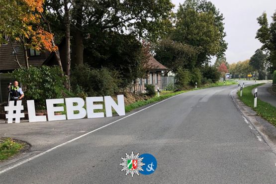 #LEBEN steht am linken Fahrbahnrand einer Landstraße in großen weißen Buchstaben 