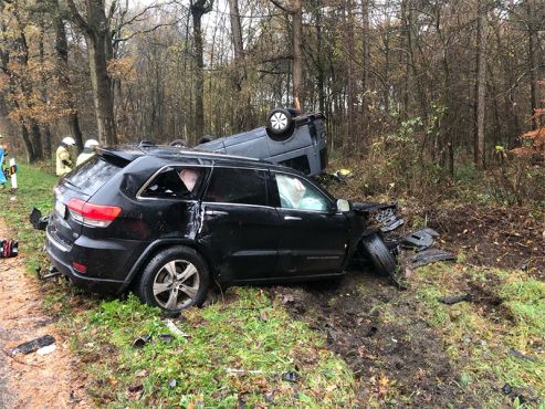 Auf dem Bild ist ein schwarzer Jeep zu sehen, der bei einem Unfall stark beschädigt wurde. Hinter ihm liegt ein Transporter auf dem Dach, der ebenfalls beschädigt wurde. Mehrere Personen wurden bei dem Unfall in Greven verletzt.