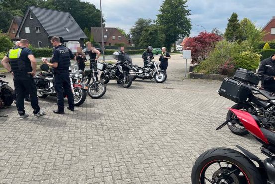 mehrere Motorräder auf einem Parkplatz in Reihe geparkt. Daneben stehen Polizisten, die die Kräder kontrollieren.